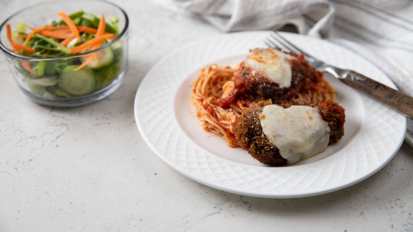 Two slices of cheese topped fried venison on a bed of pasta.
