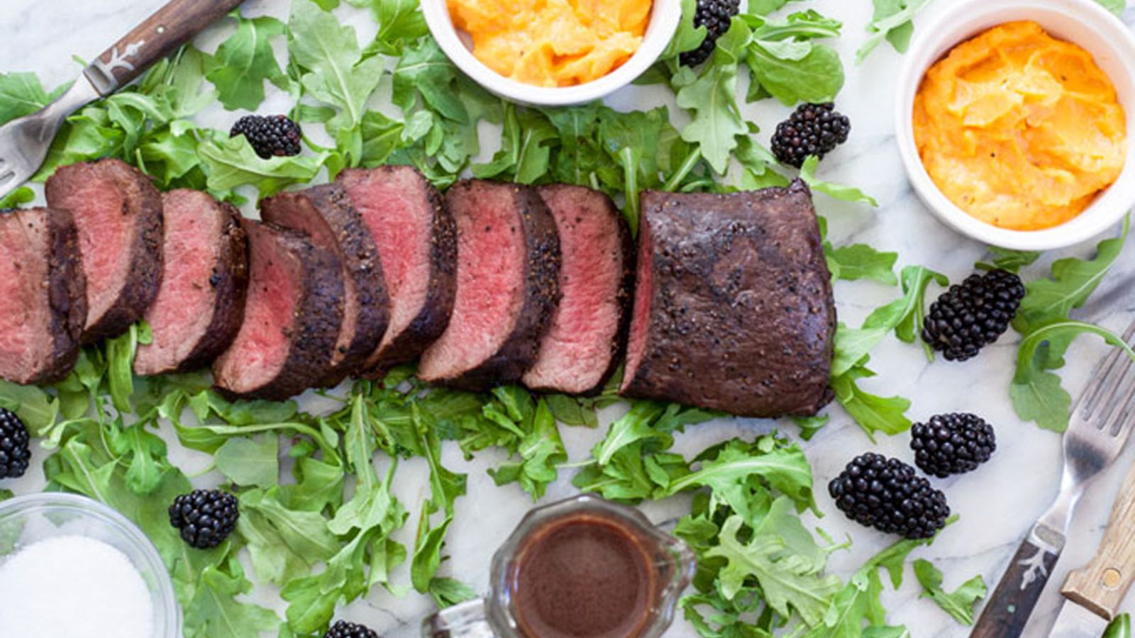 Sliced venison loin with blackberries. on a bed of arugula.