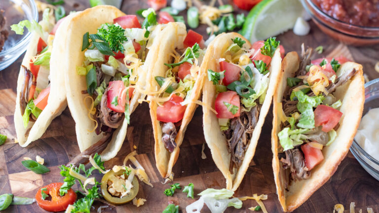 Brisket tacos, standing on a wooden board with scattered toppings.