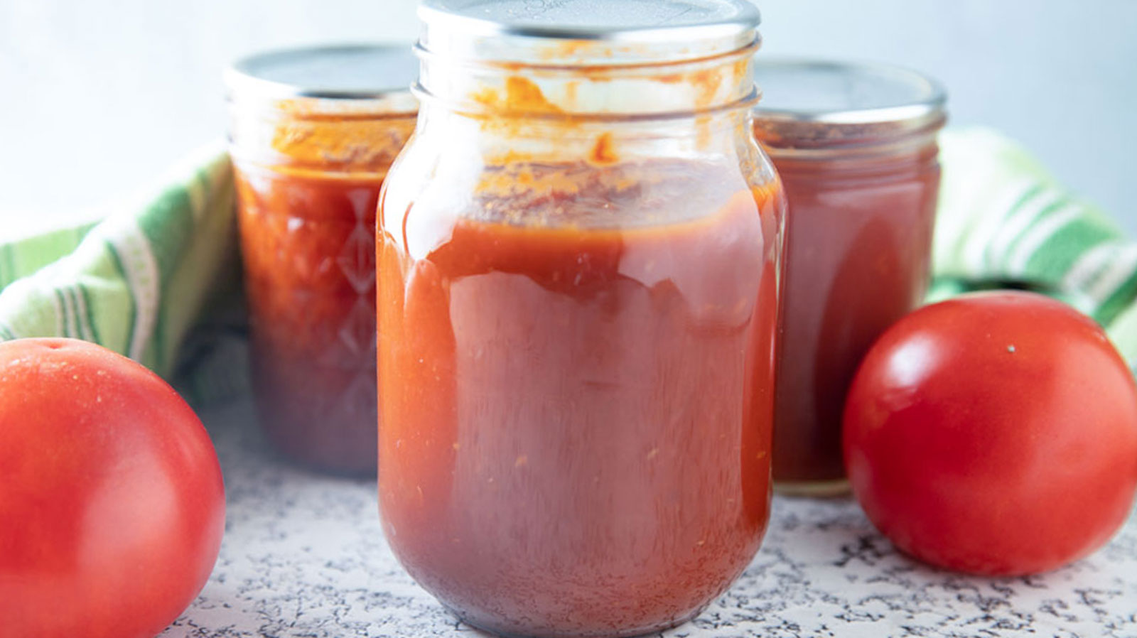 Pint jar with tomato ketchup with fresh tomatoes and a green towel.