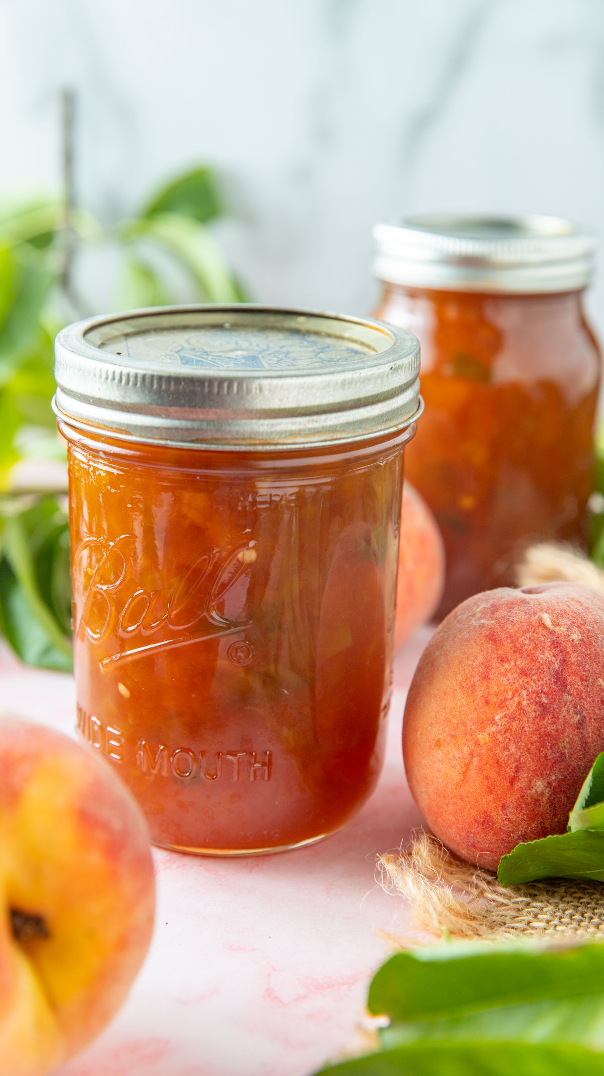 Jars of peach jam with fresh peaches and peach tree leaves.