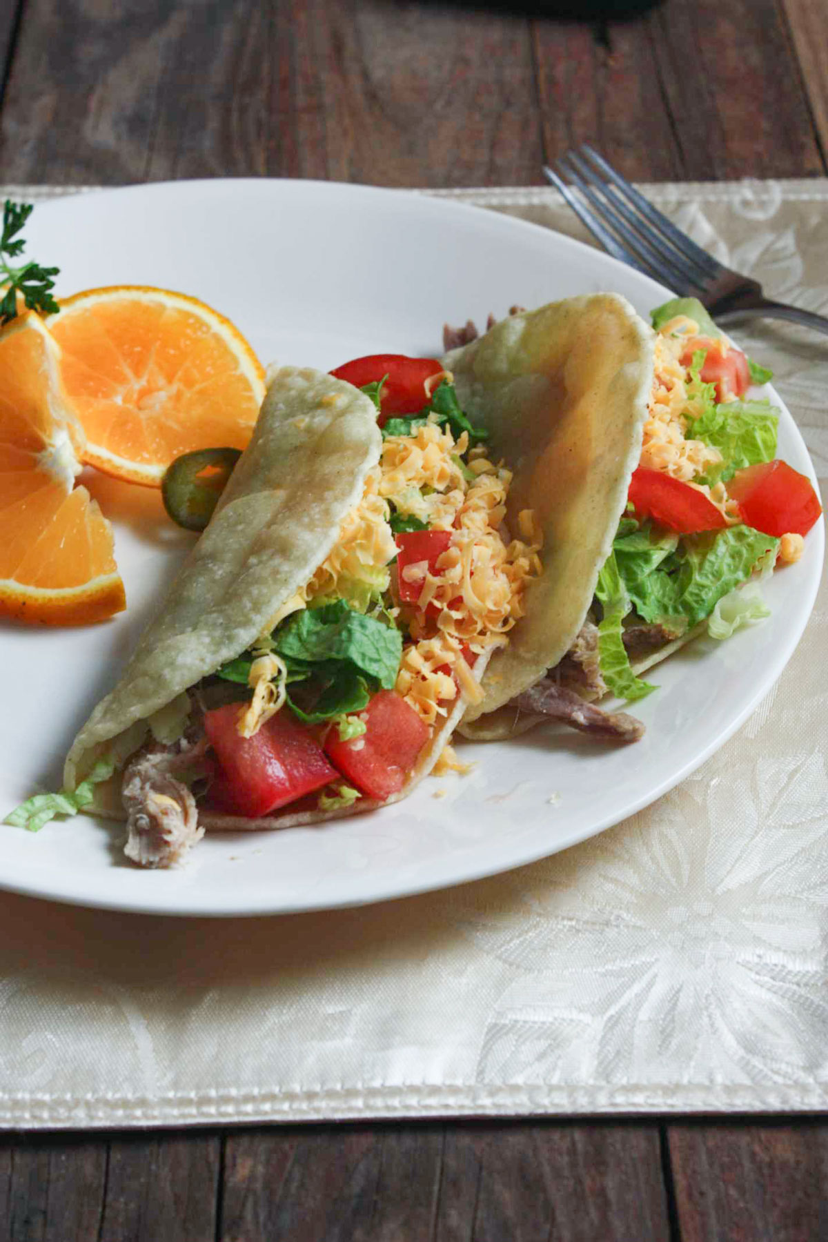 Pork sticking out of tacos on a white plate.