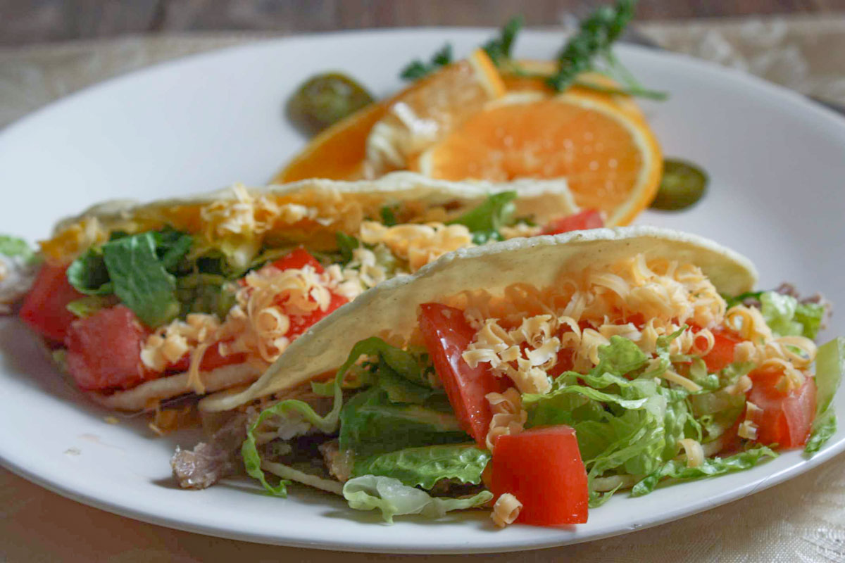 Two tacos topped with lettuce, tomato and cheese.