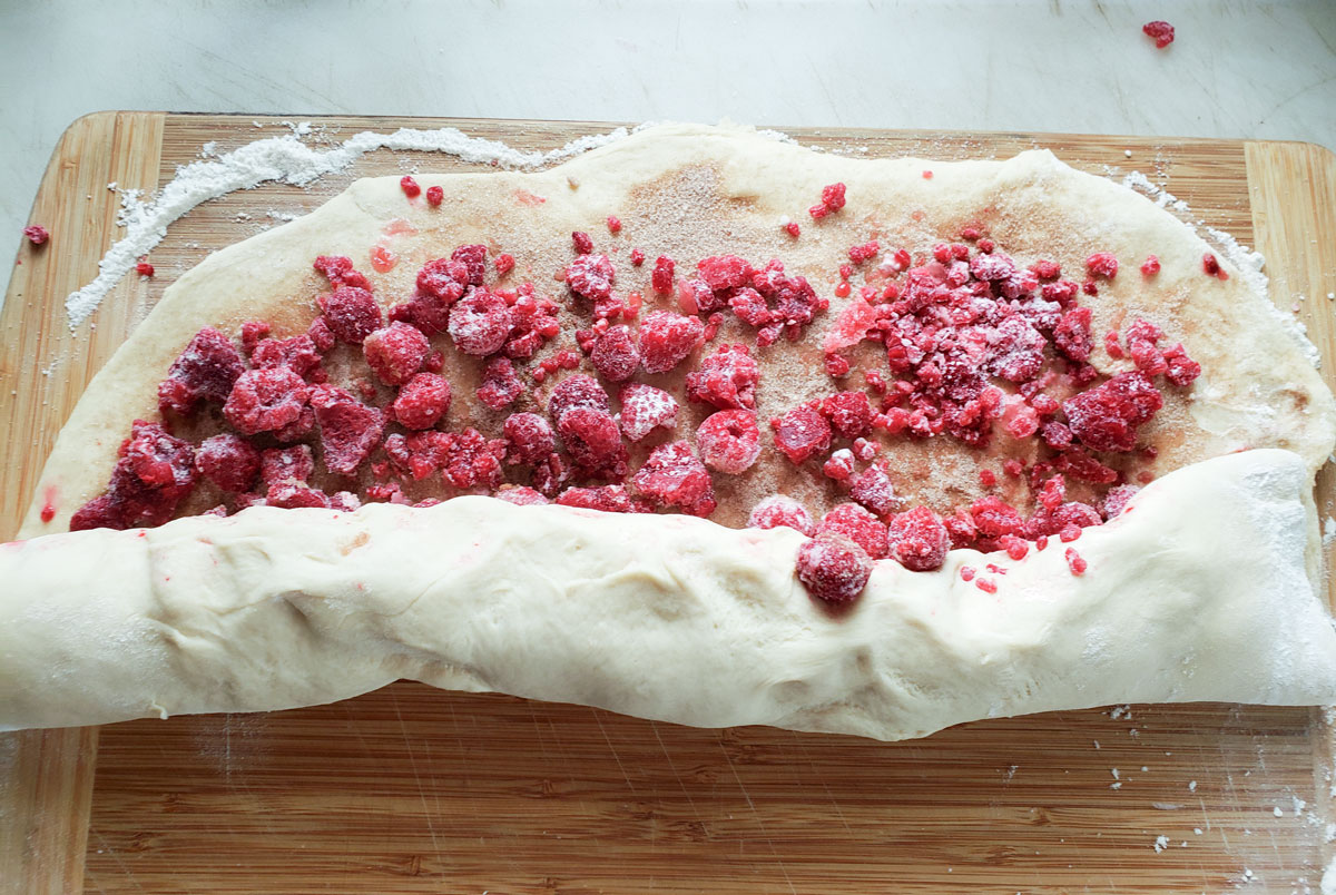 Dough sprinkled with cinnamon sugar and raspberries and started to be rolled up.
