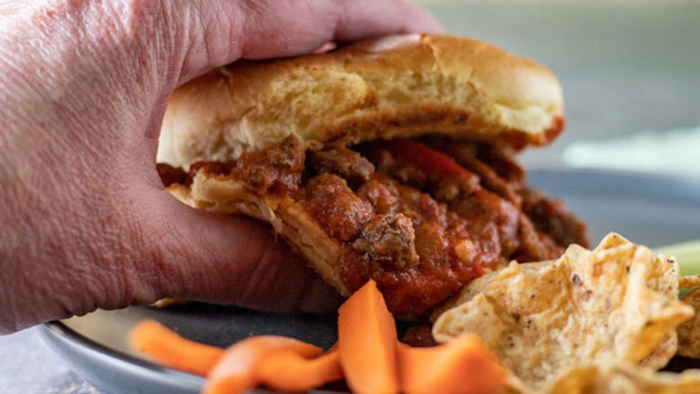 Close up of woman's hand picking up a sloppy Joe.