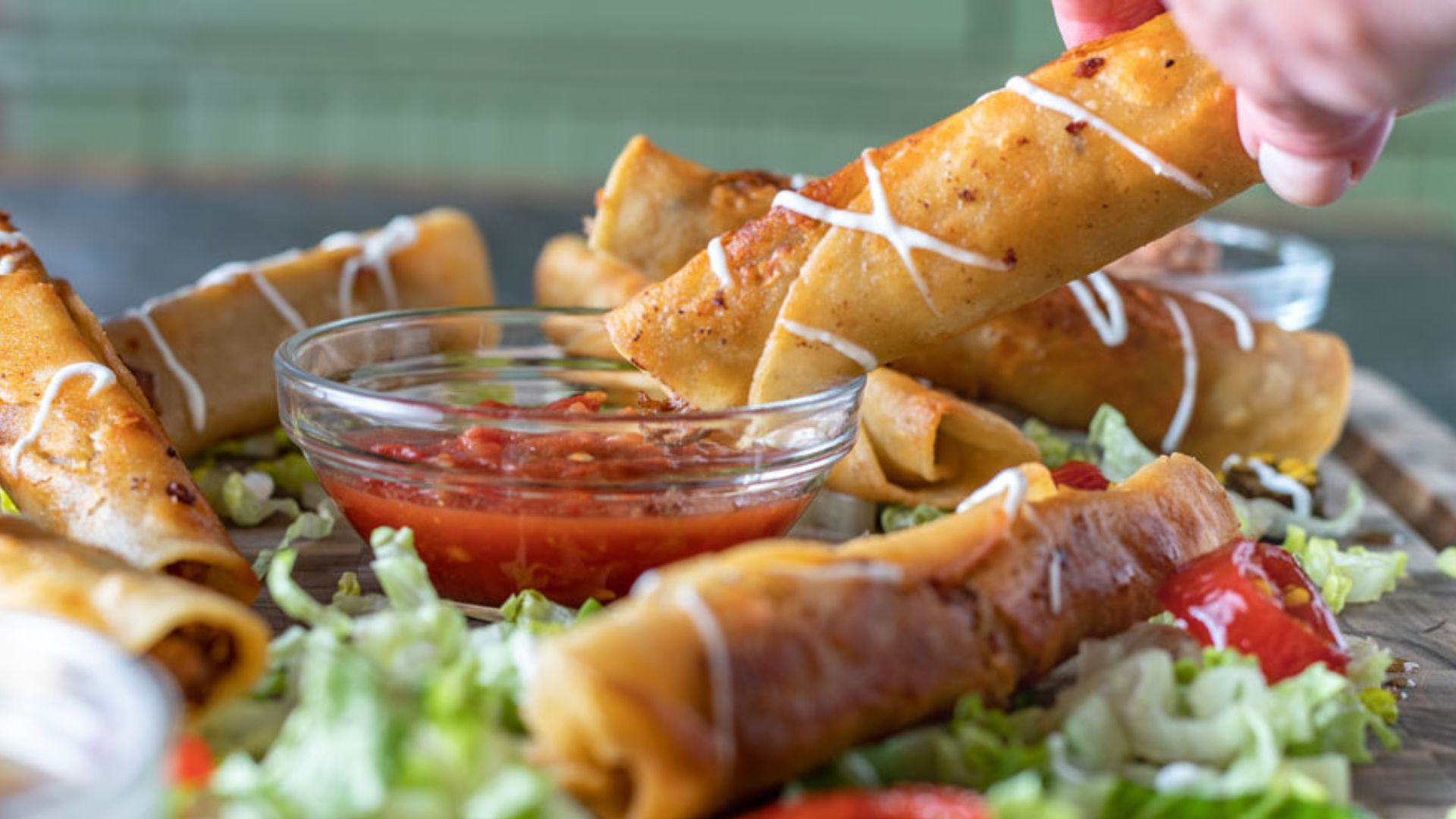 Close up of woman's hand dipping taquito into a bowl of salsa.