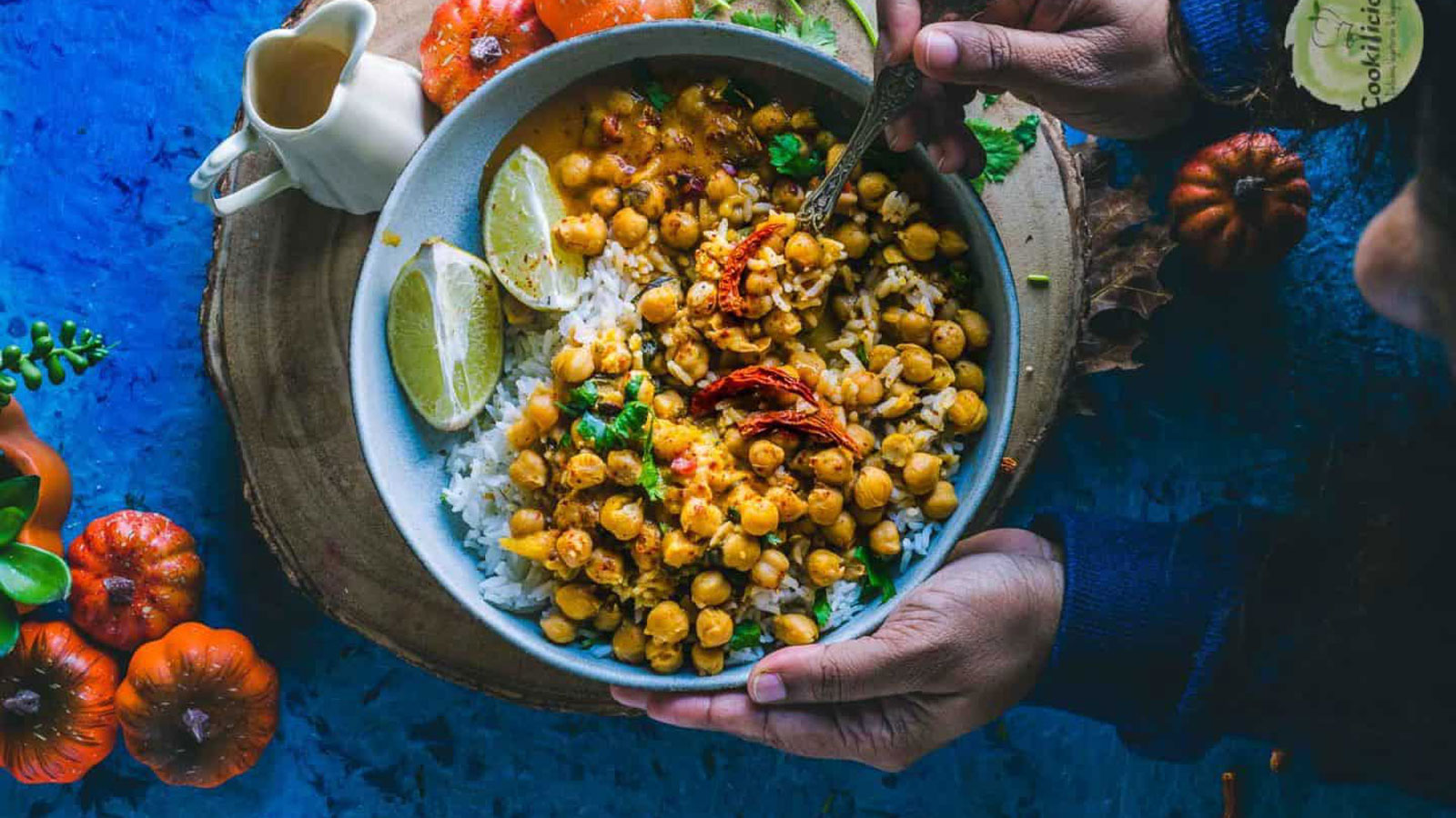 Woman's hands holding a large bowl of colorful curry.