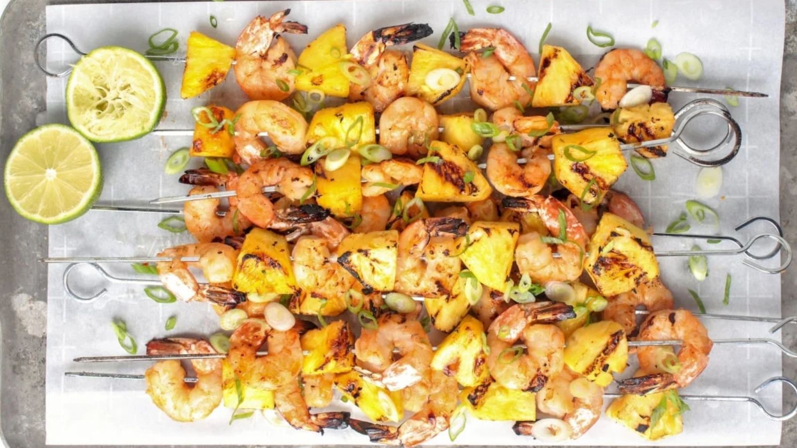 Shrimp and pineapple skewers with sliced limes.