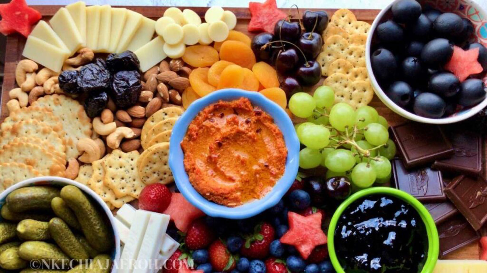 Nuts, fruit, pickles, and dips on a board.