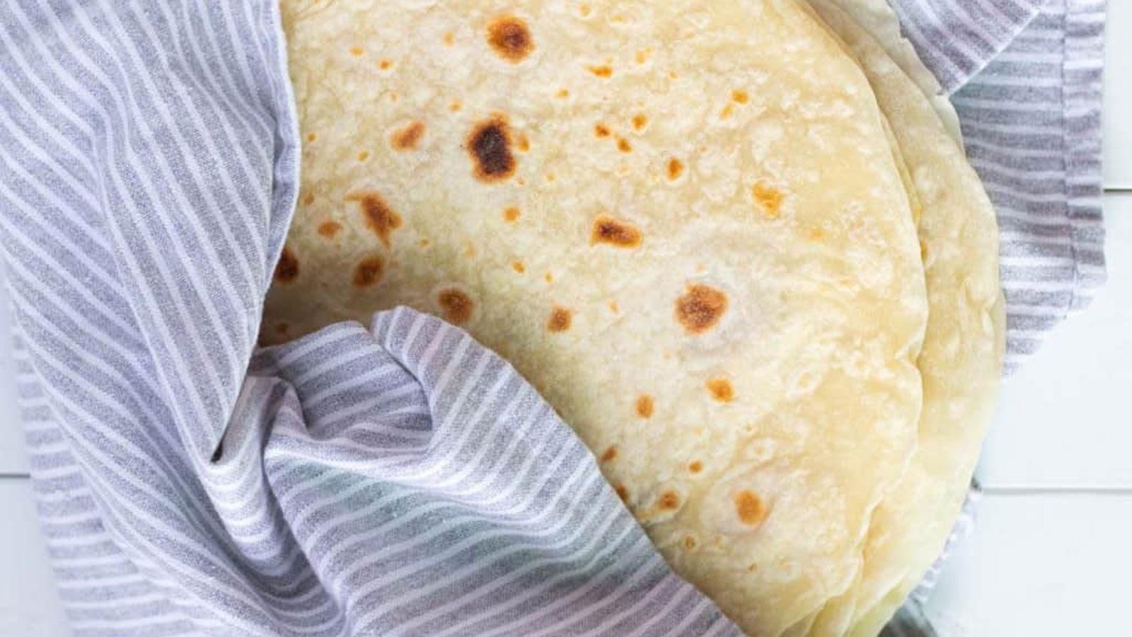 Flour tortillas wrapped in a purple and white striped towel.