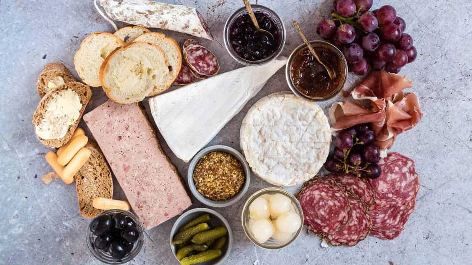 Chunks on meats, cheese, and pickles on a gray board.