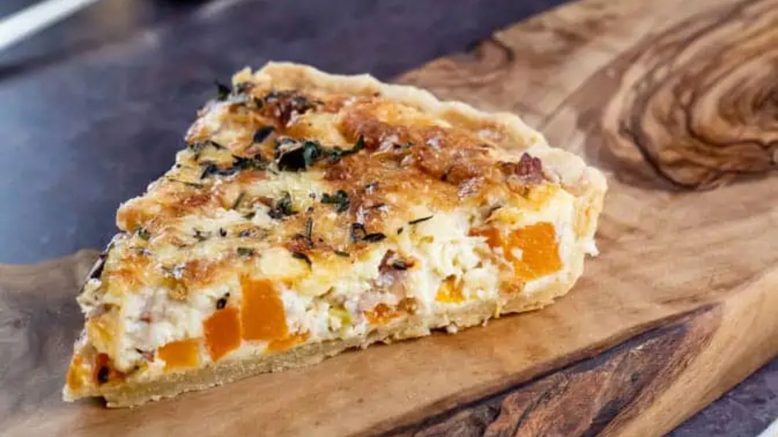A slice of leek and squash quiche on a wooden board.