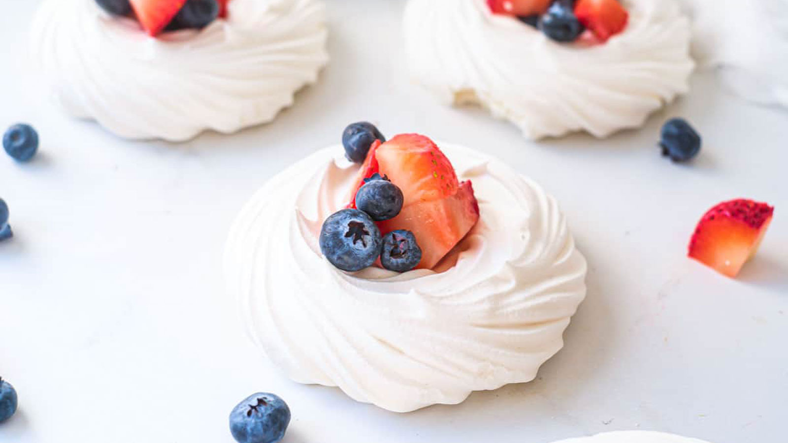 White pavlovas with strawberries and blueberries.