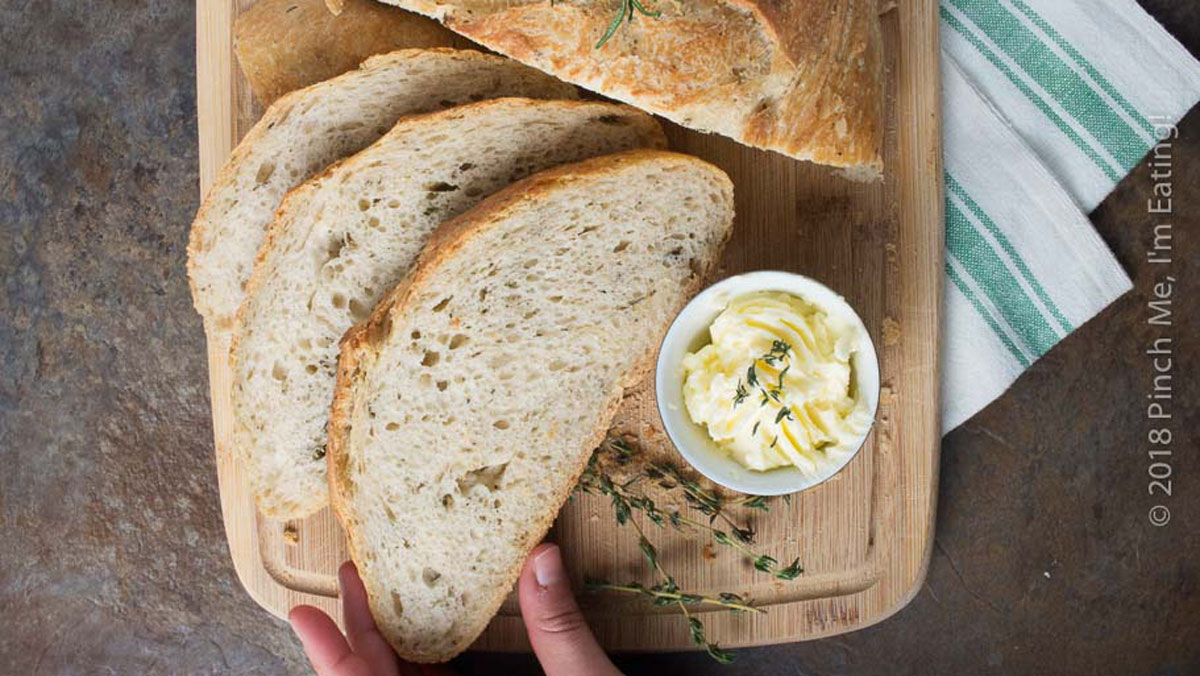 Sliced sourdough loaf with woman's hand grabbing a piece.