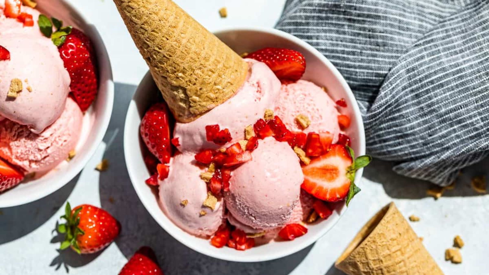Strawberry ice cream in a bowl with cones on the side.
