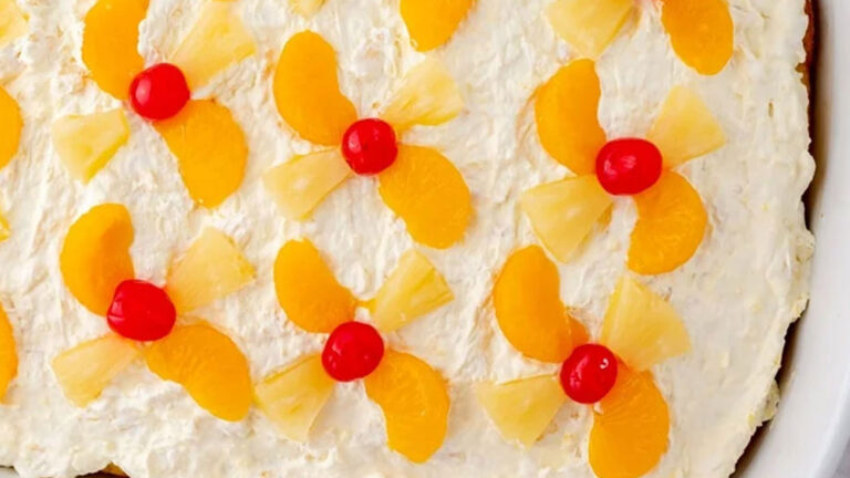 Cake with white icing and garnished with cherries and oranges.