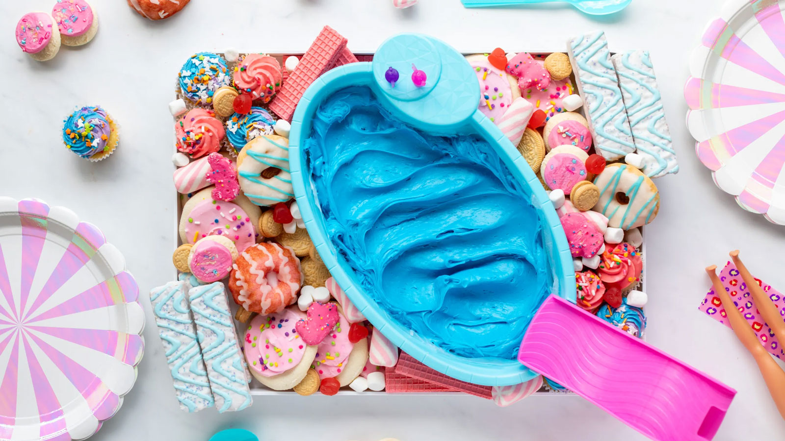 Blue frosting in a blue bowl with pink cookies and decorations.