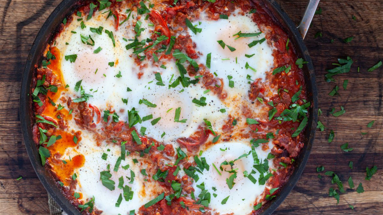 Eggs in a cast iron skillet with tomato sauce. and garnished with chopped greens.