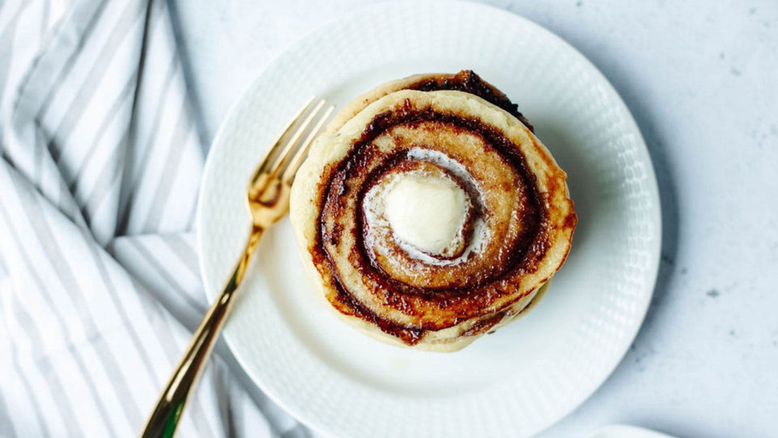 Stack of pancakes on a white plate with a pat of butter.