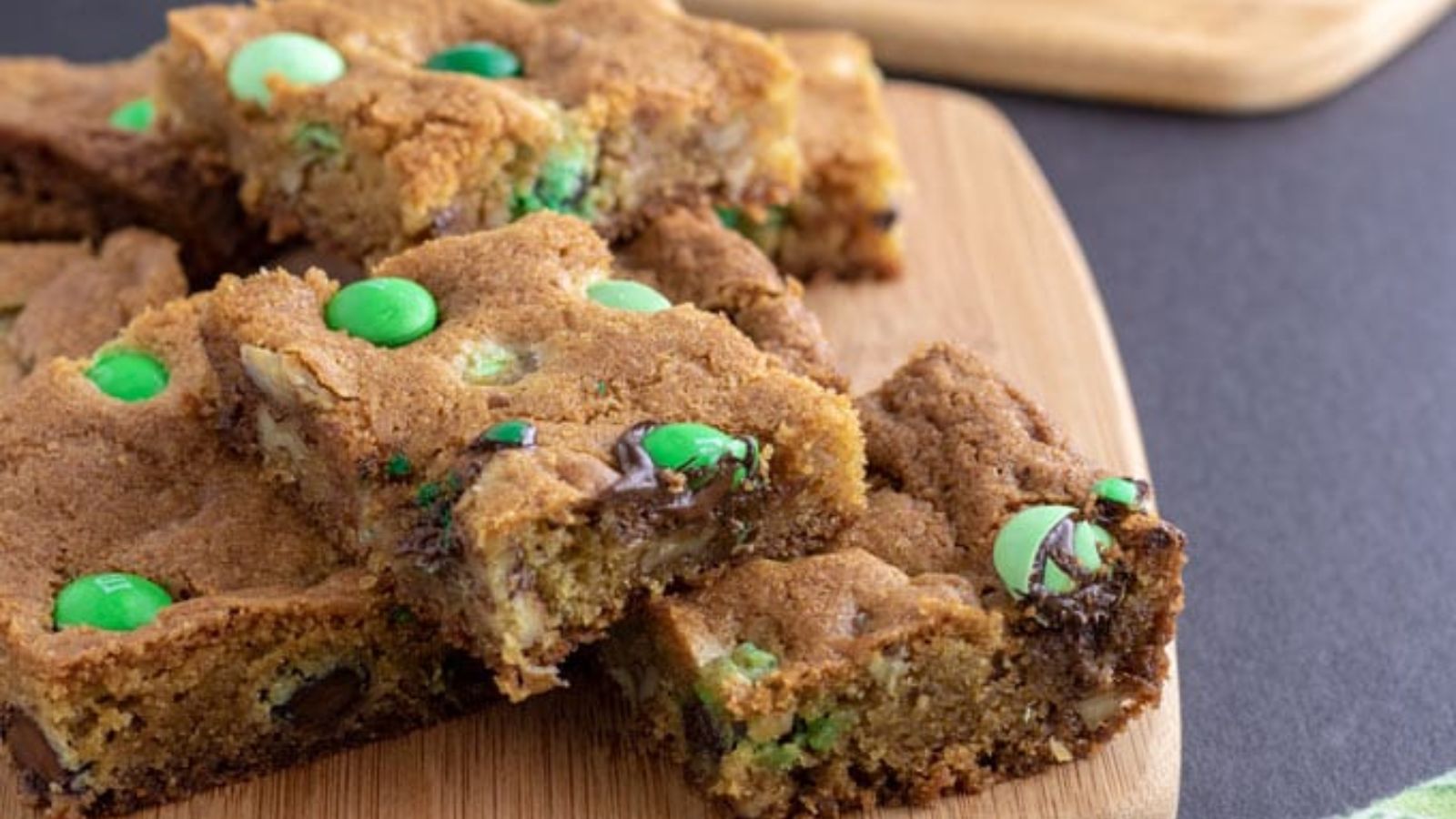 M&M cookie bars stacked on wooden board.