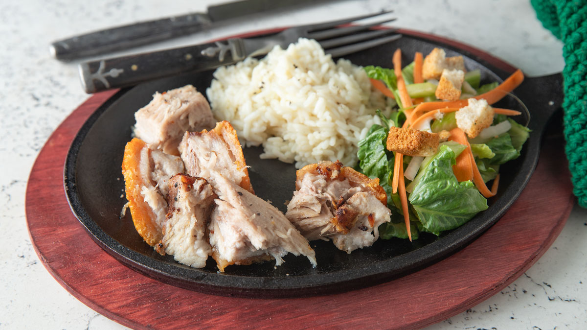 Chunks of pork belly with rice and salad.
