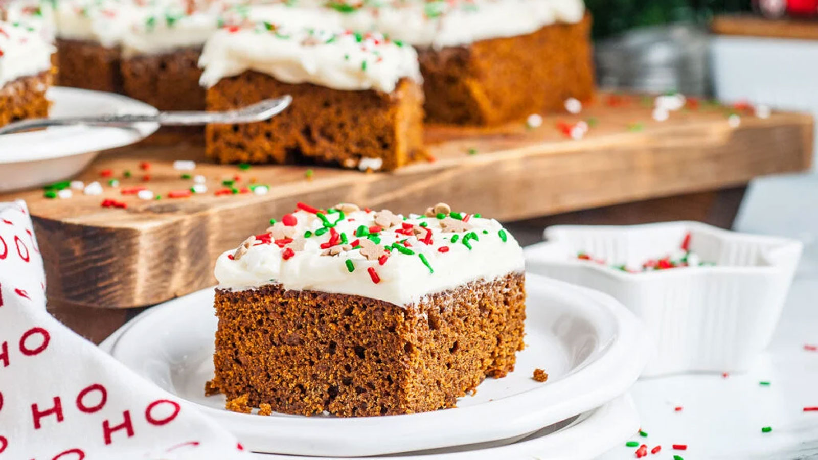 Piece of ginger cake with white frosting and sprinkles on a white plate.