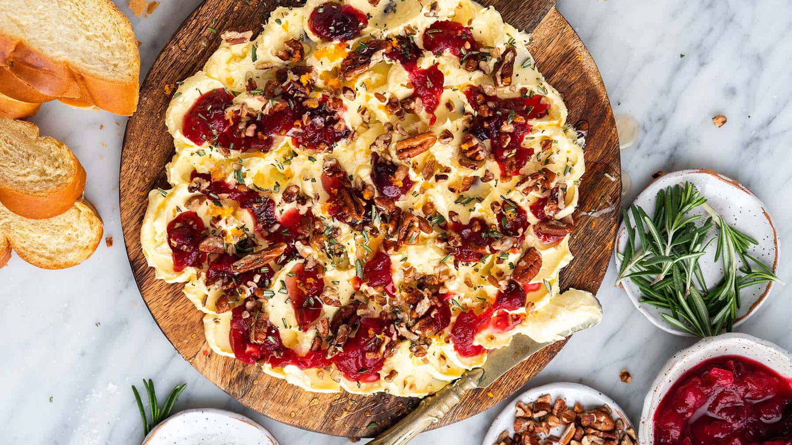 Whipped butter spread on a board with sauces, nuts, and herbs. 