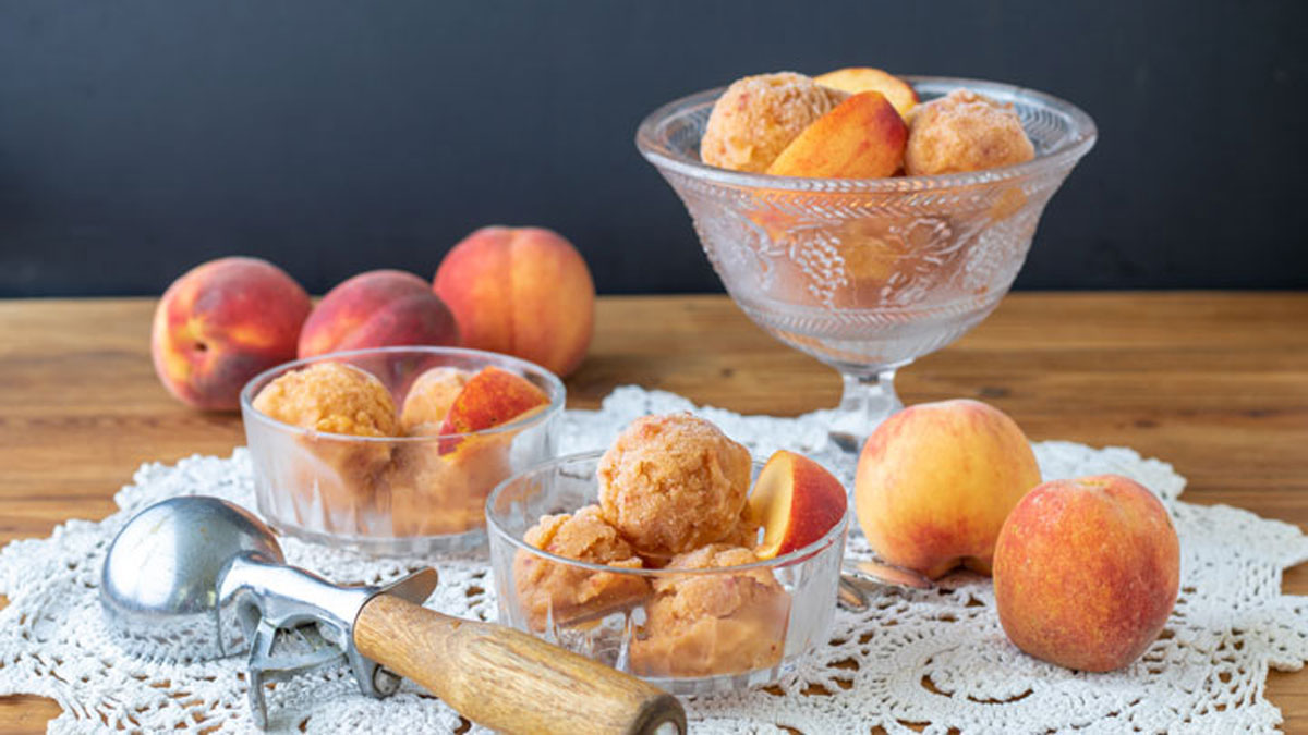 Peach sorbet in goblet with bowls and peaches.