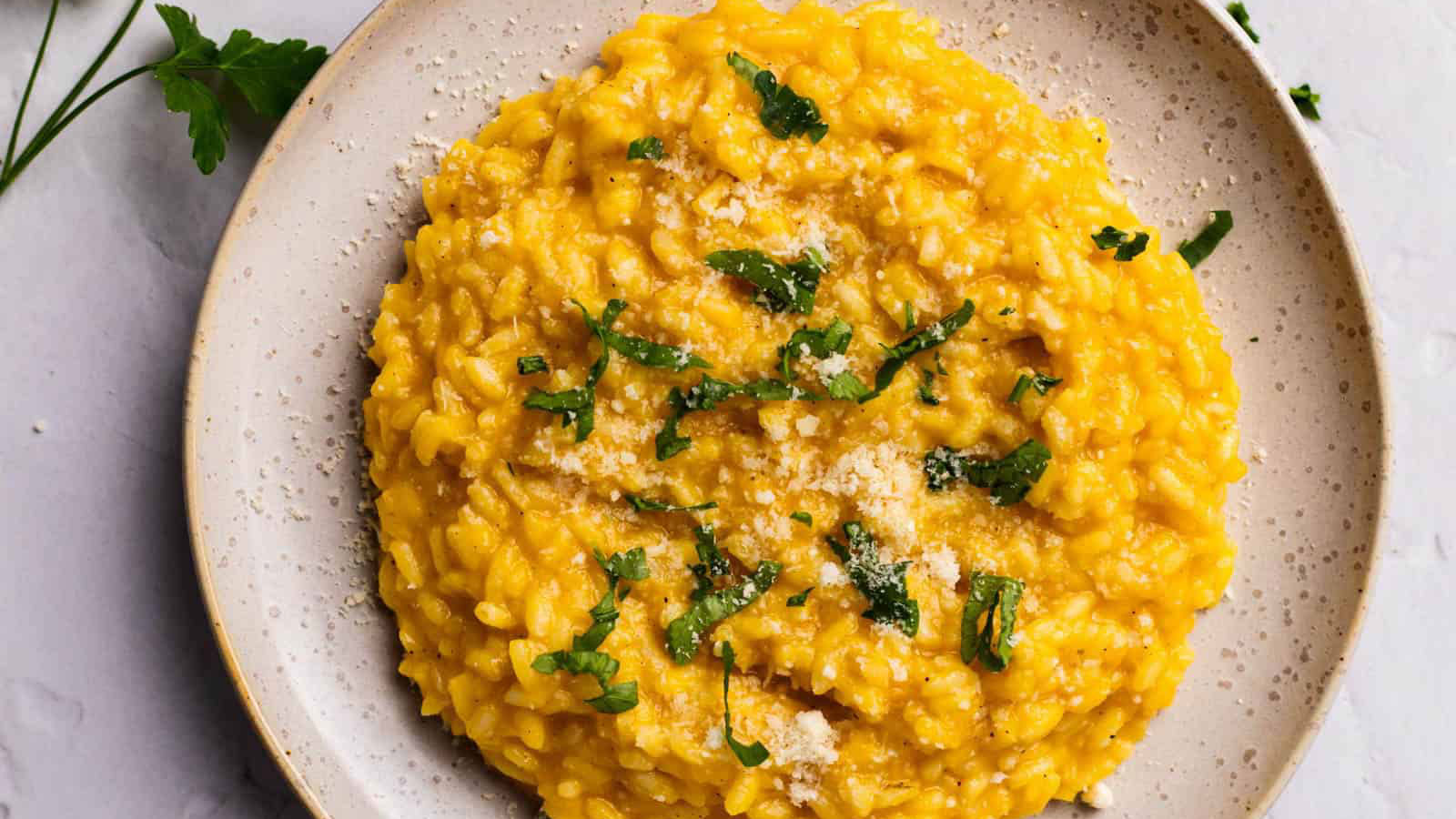Colorful pumpkin risotto on a beige plate garnished with parsley.