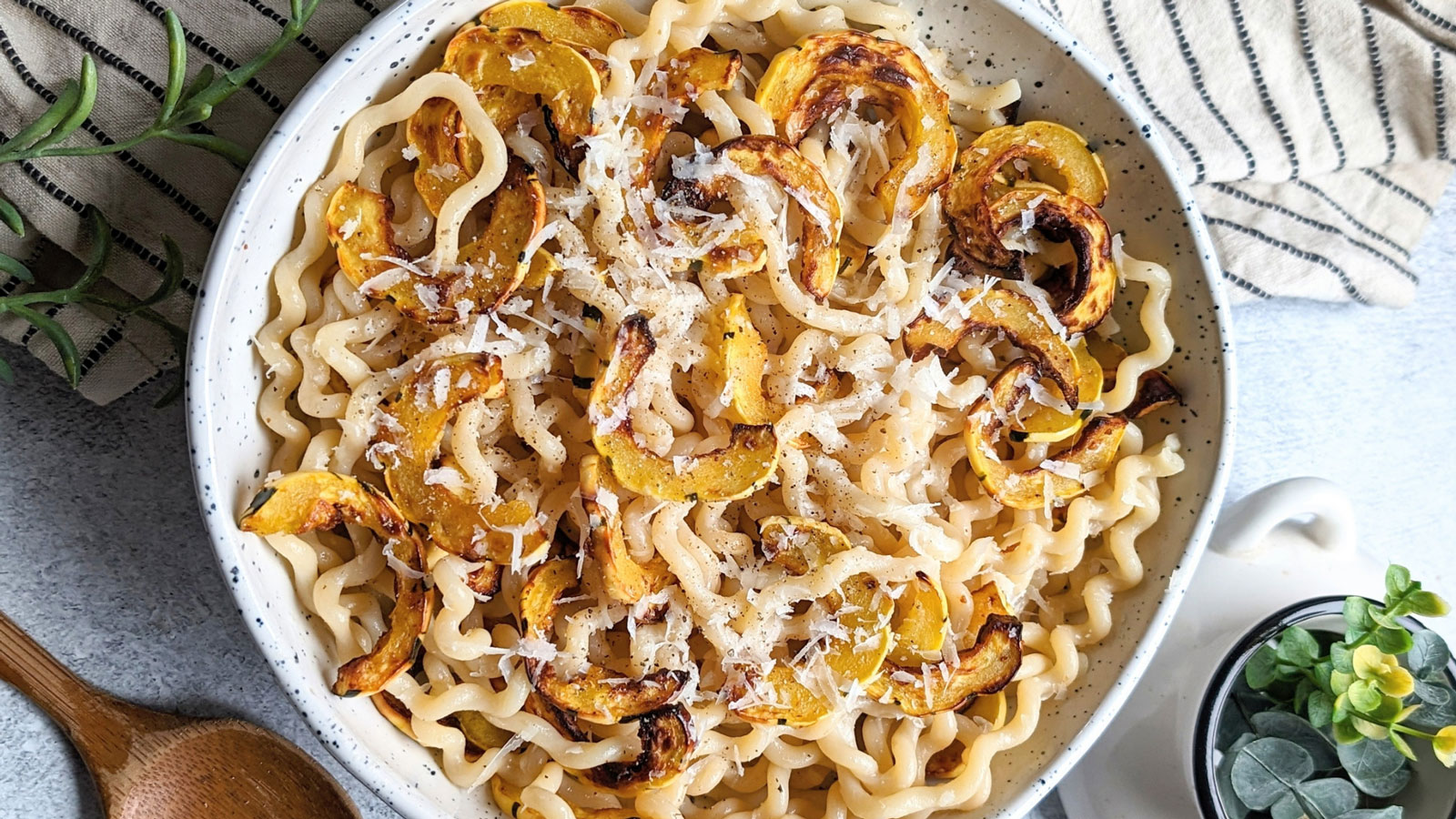Fusilli pasta with roasted squash and cheese in a white bowl.