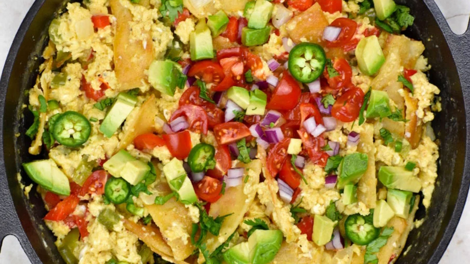 Colorful veggie topped scrambled eggs in a cast iron skillet.