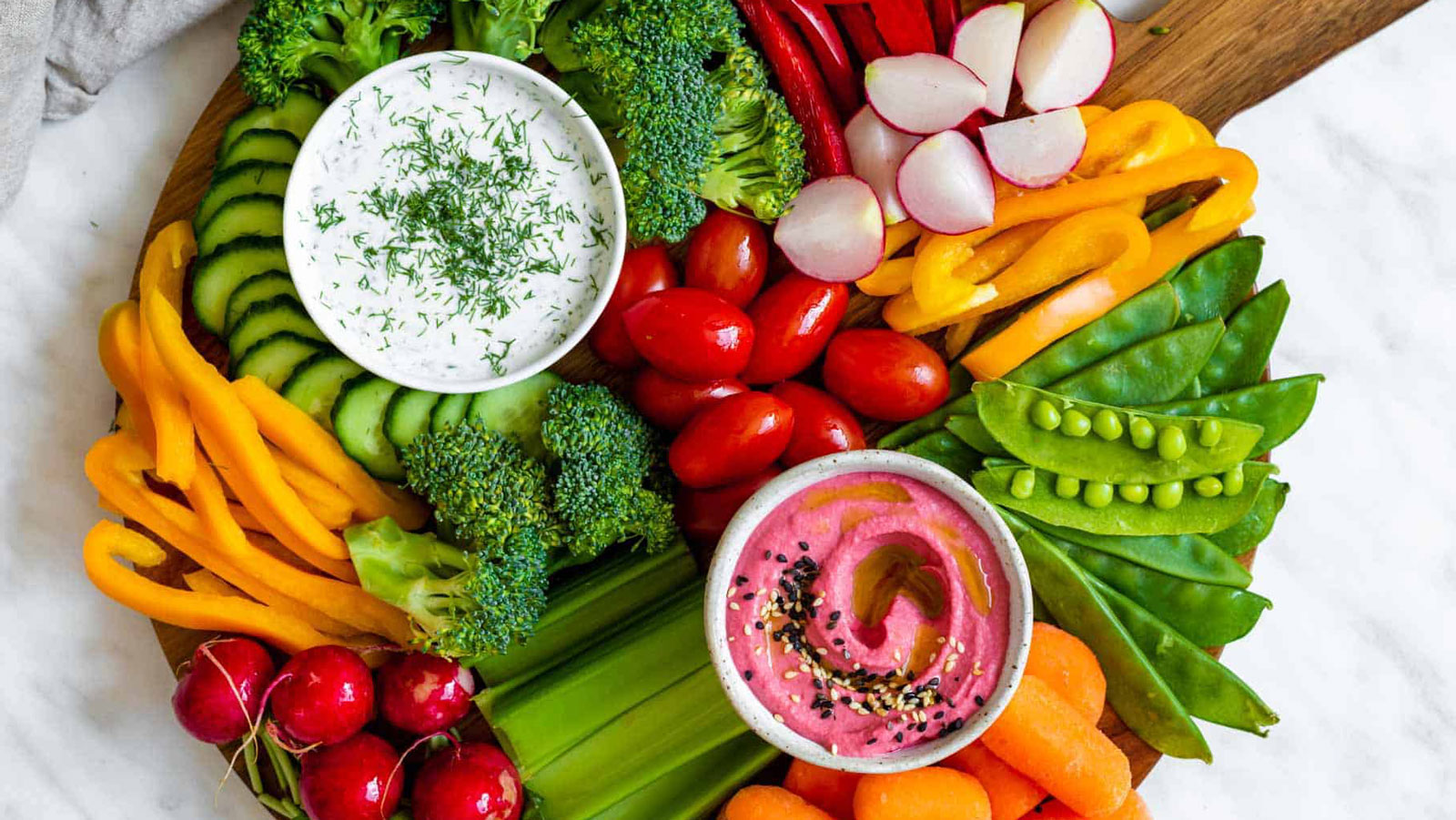Vegetables and dips on a round cutting board.