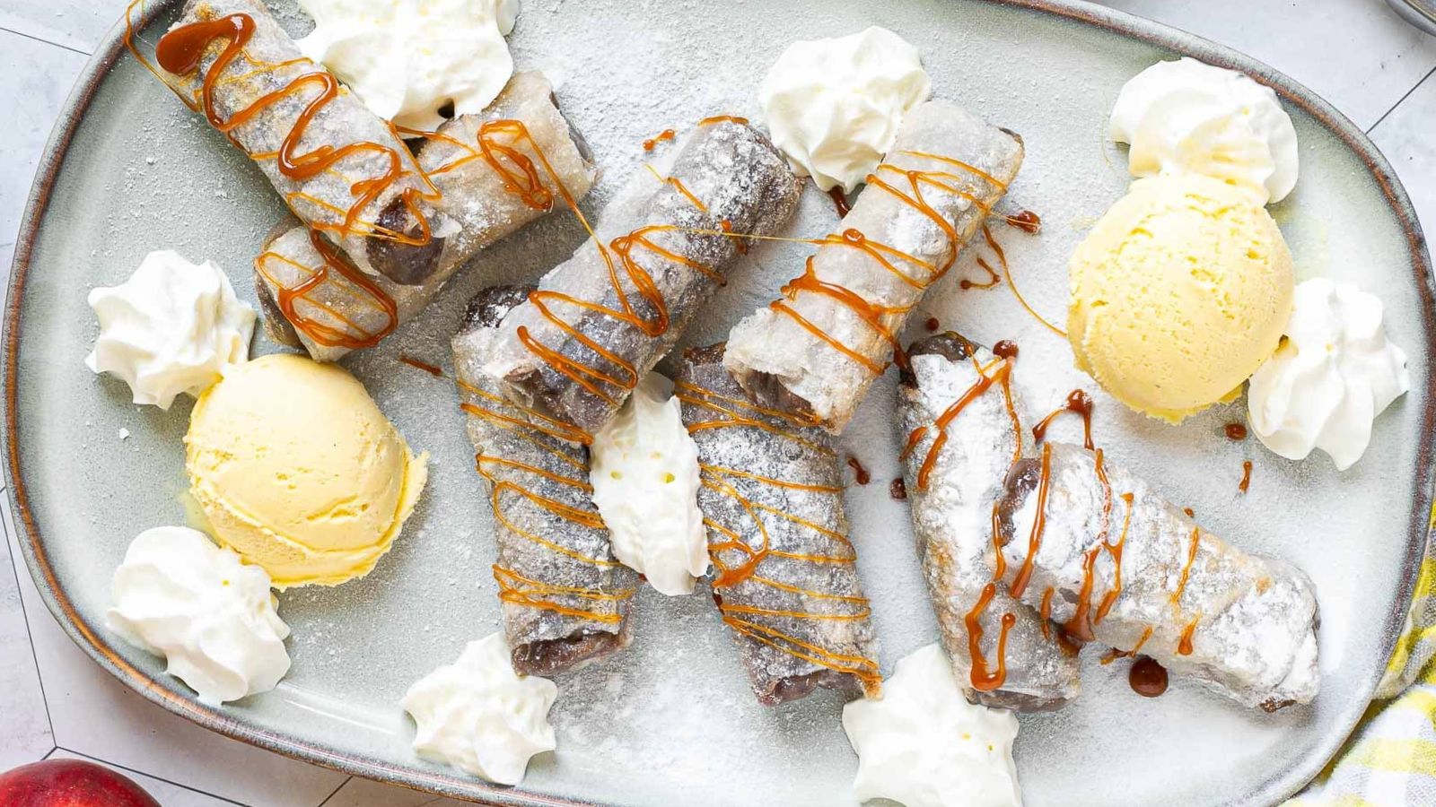 Apple pie spring rolls on a big plate with scoops of ice cream.