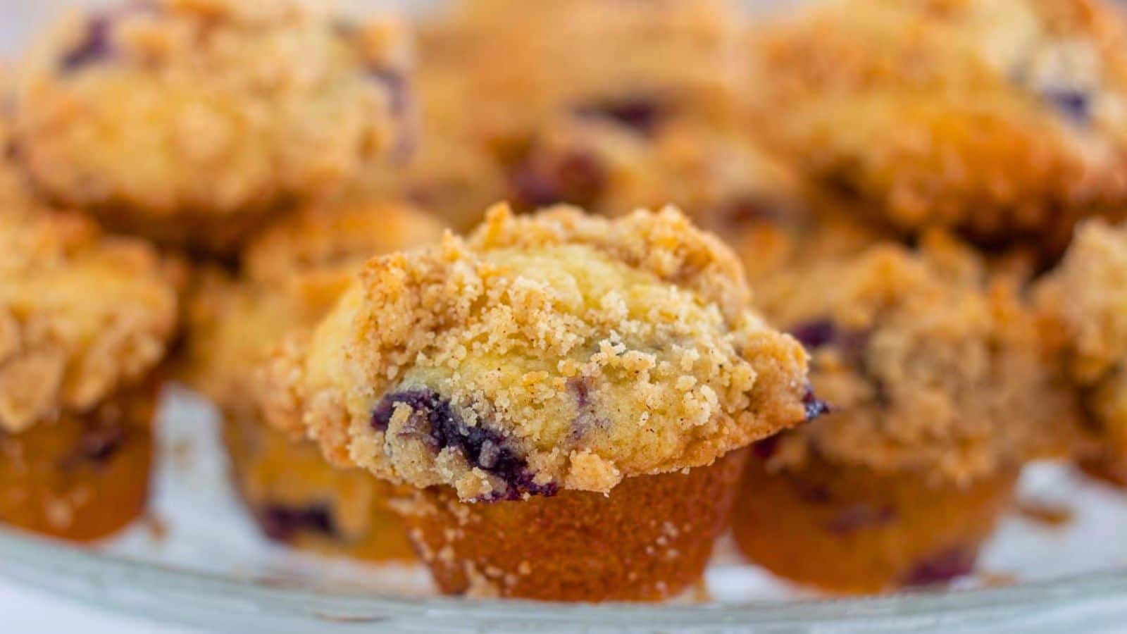 Blueberry muffins topped with a crunchy streusel topping on a white plate.