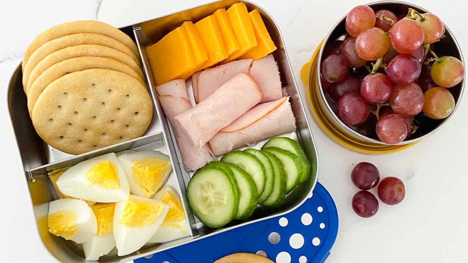 Bento lunch with crackers, cheese, turkey and grapes.