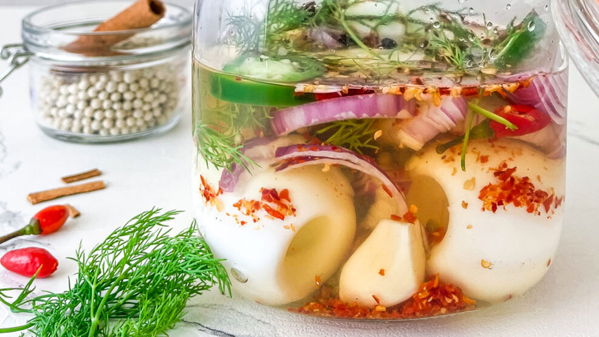 Pickled eggs in a jar with colorful herbs and peppers.