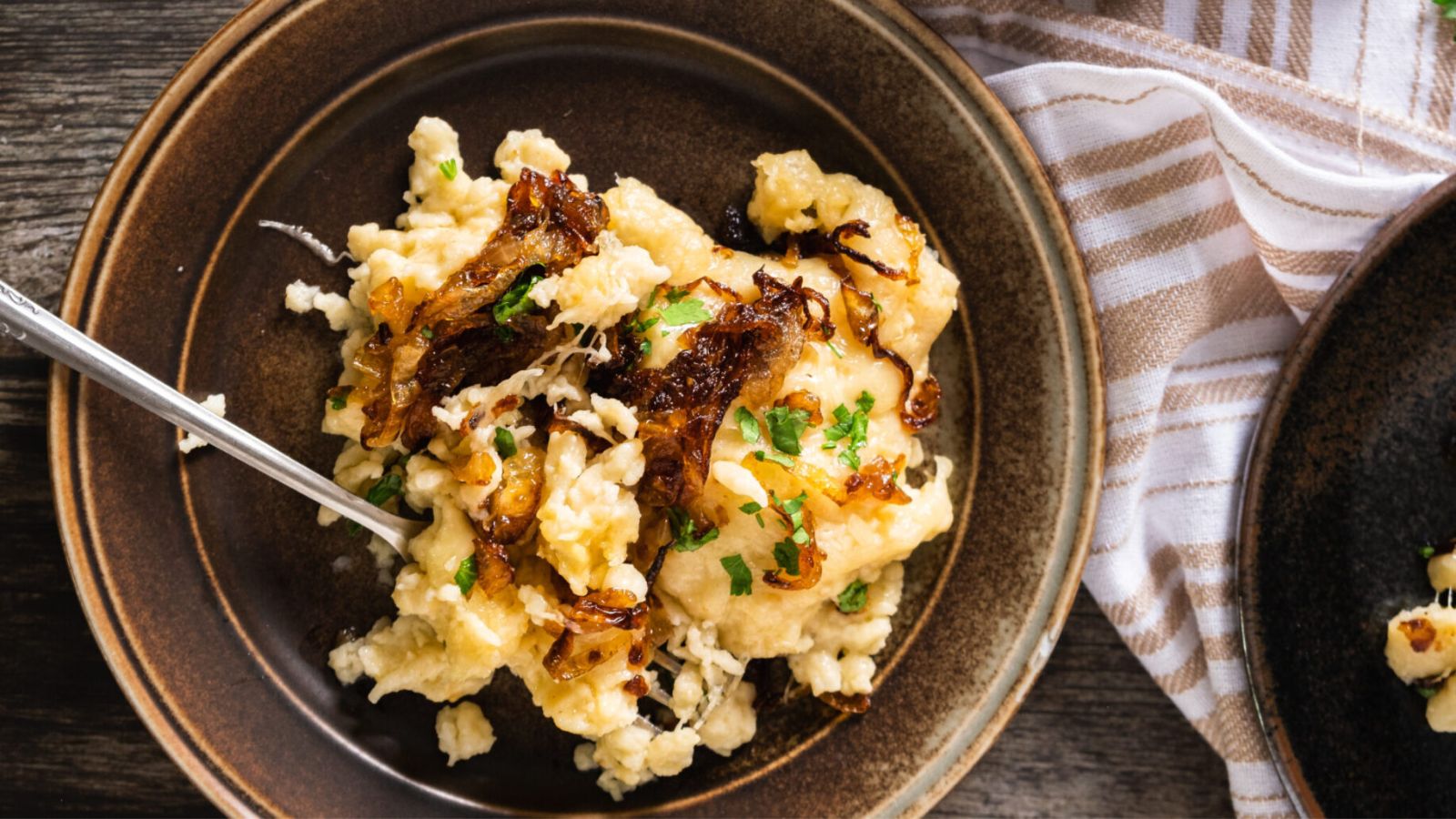 Spaetzle on a brown plate with caramelized onions and cheese.