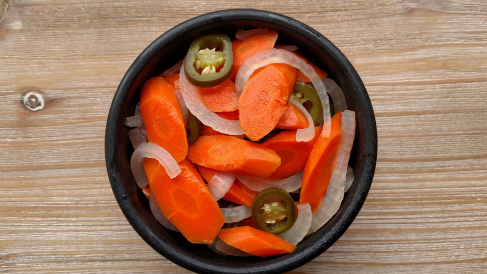 Black bowl with carrots, onions and jalapeno.