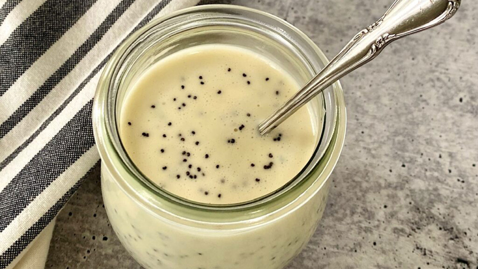 Poppy seed dressing in a jar with a spoon in it.