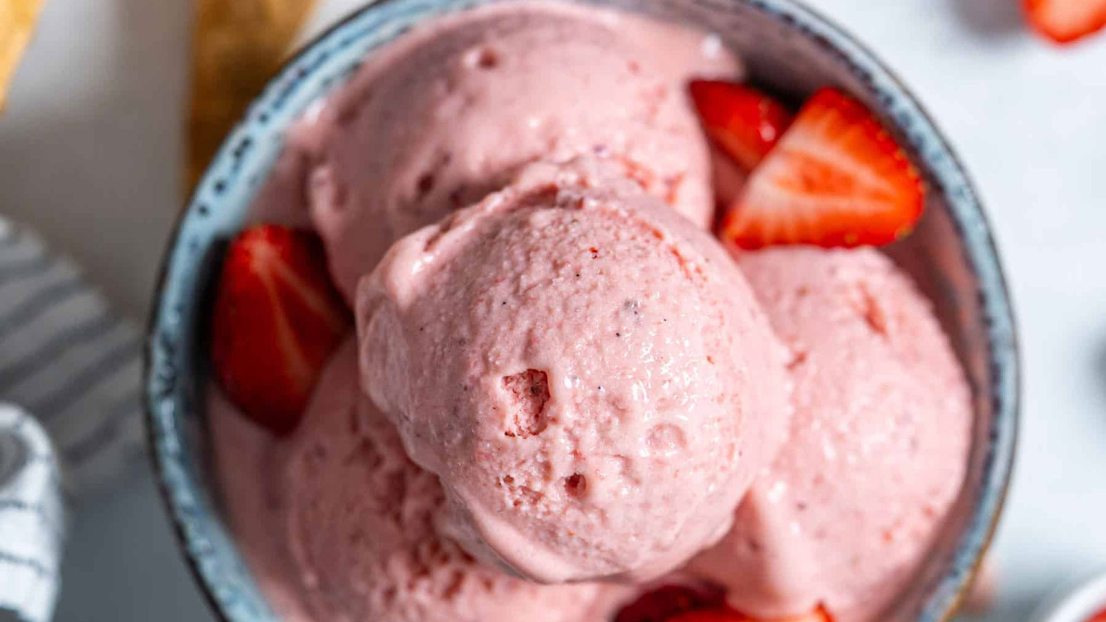  Blue bowl filled with scoops of strawberry ice cream topped with chopped berries.