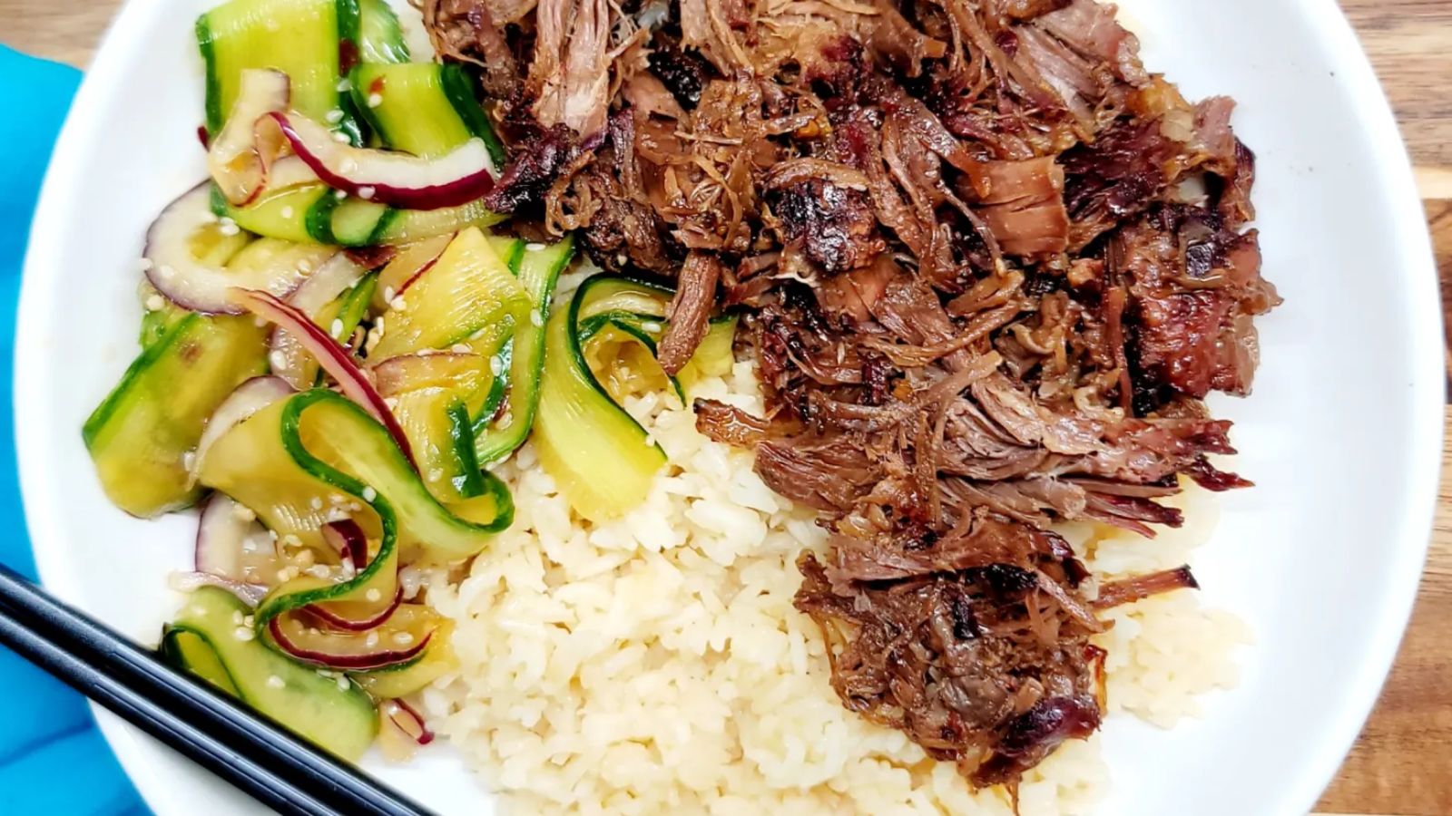 Spicy Cucumber salad on  a plate with rice and meat on the side.