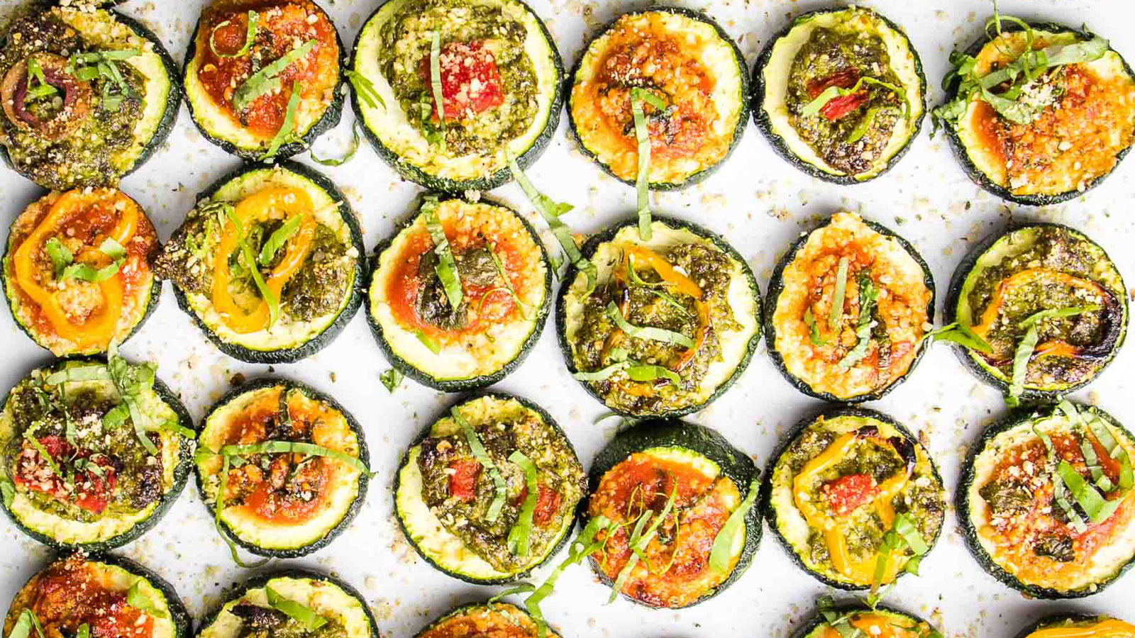 Zucchini pizza bites on a white board with colorful toppings.