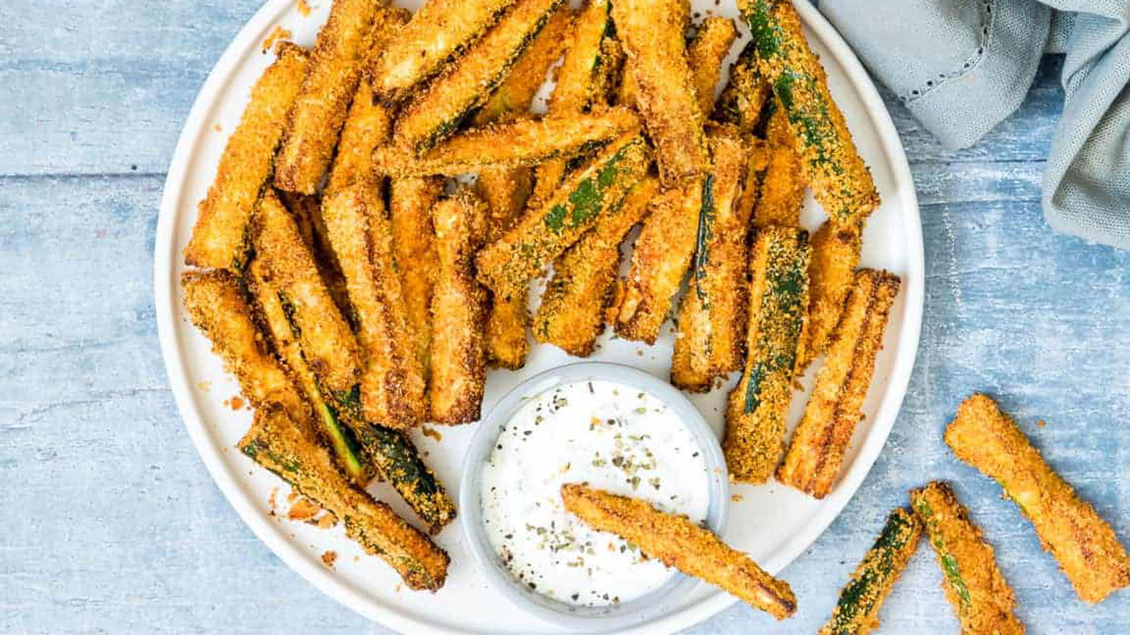 White plate loaded with zucchini fries and dipping sauce.