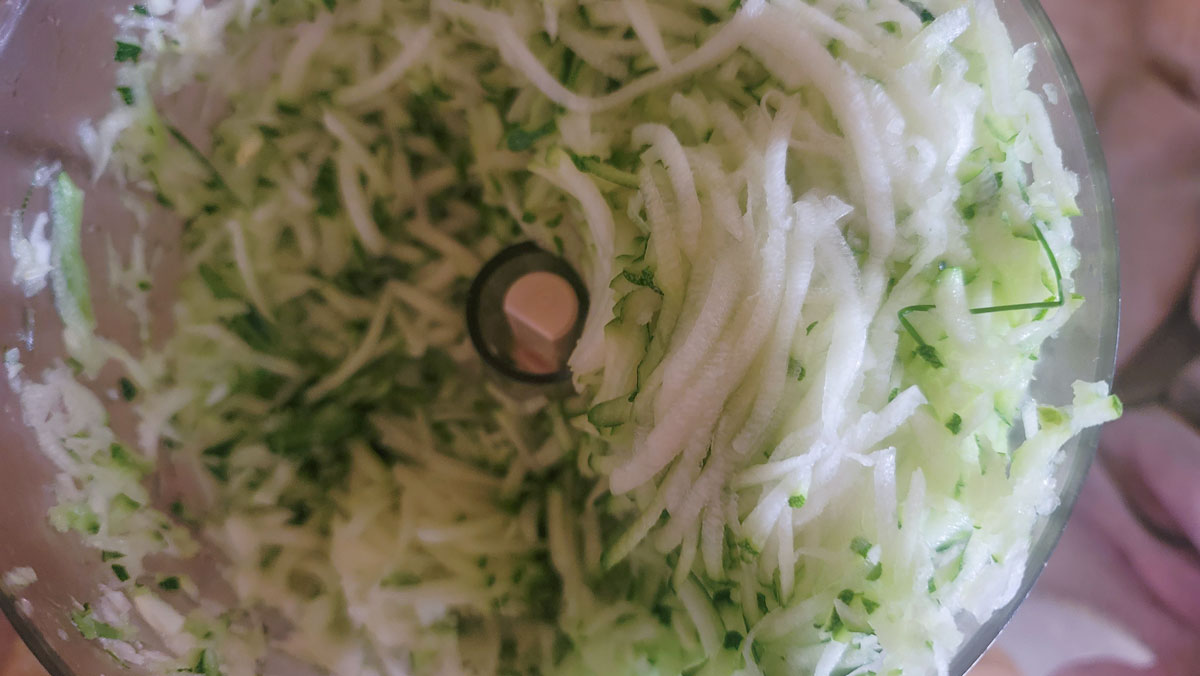 Grated zucchini in a food processor bowl.