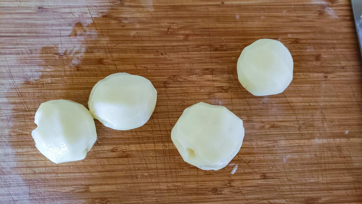 Whole, peeled potatoes on a cuttting board.