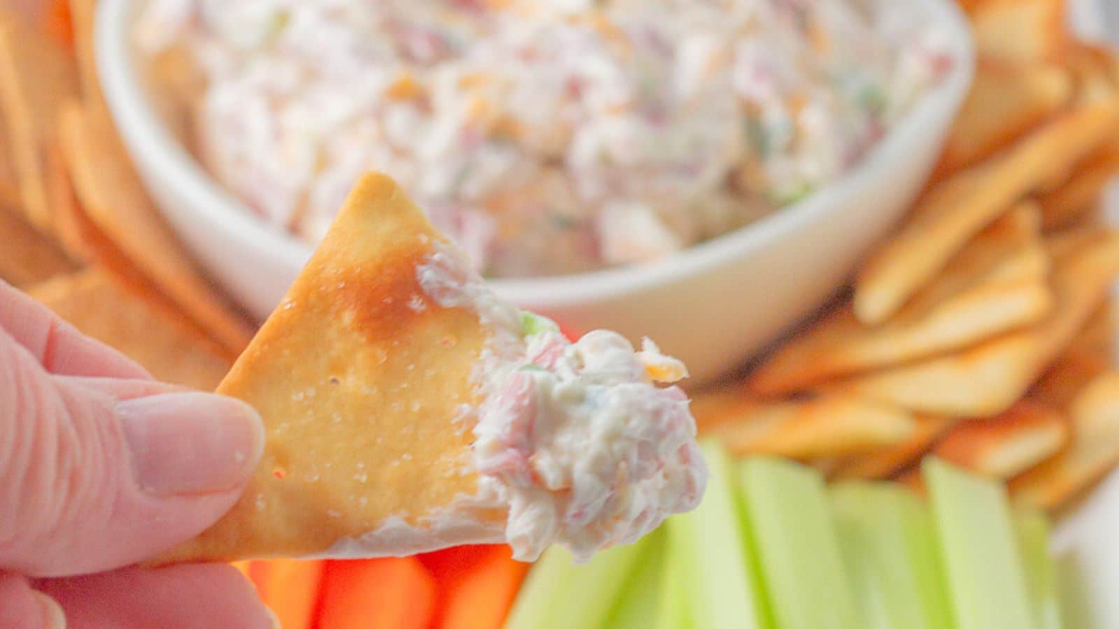 Woman's hand holding a chip that had been dipping into the dip.
