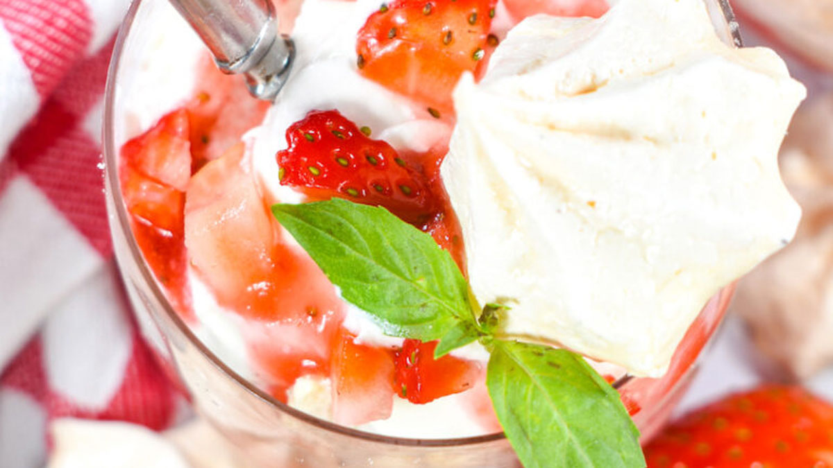 Bowl with strawberries and cream topped with basil leaf.