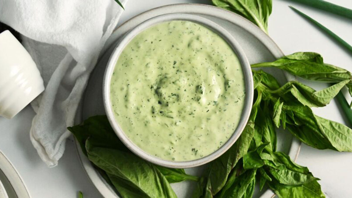 White bowl filled with green goddess dressing surrounded by greens.