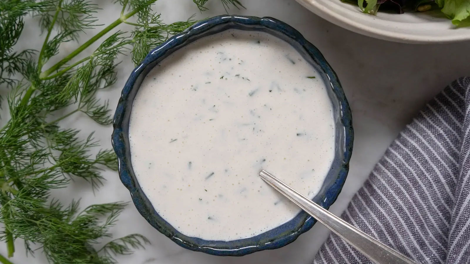 Ranch dressing in a dark blue bowl with fresh dill.