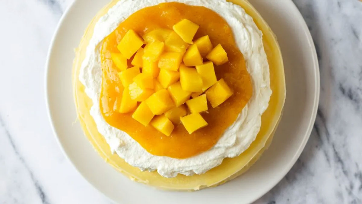 Overhead photo of a yellow cake topped with white cream and mango sauce.